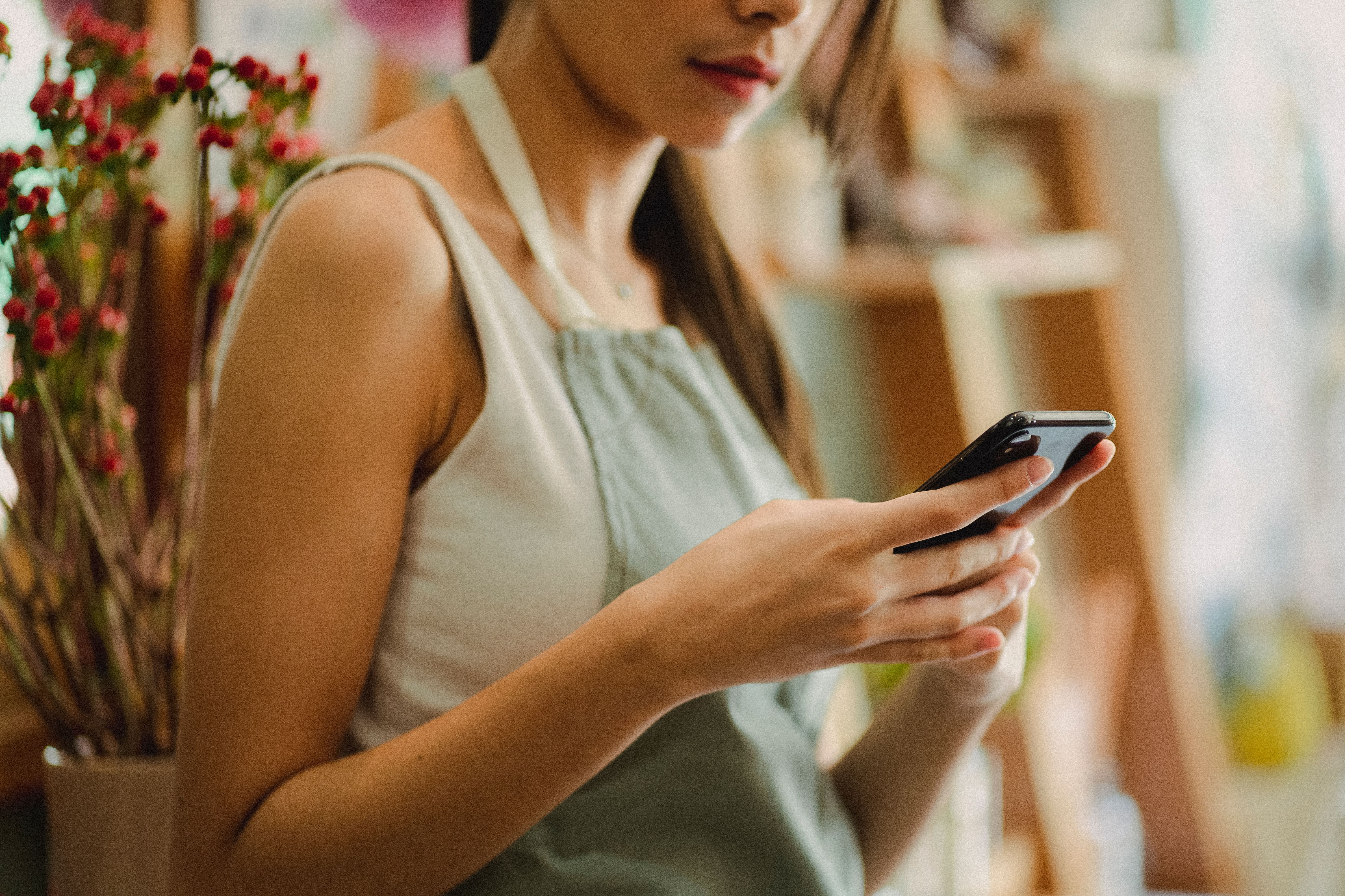 Small business florist in apron browsing a mobile phone in her shop