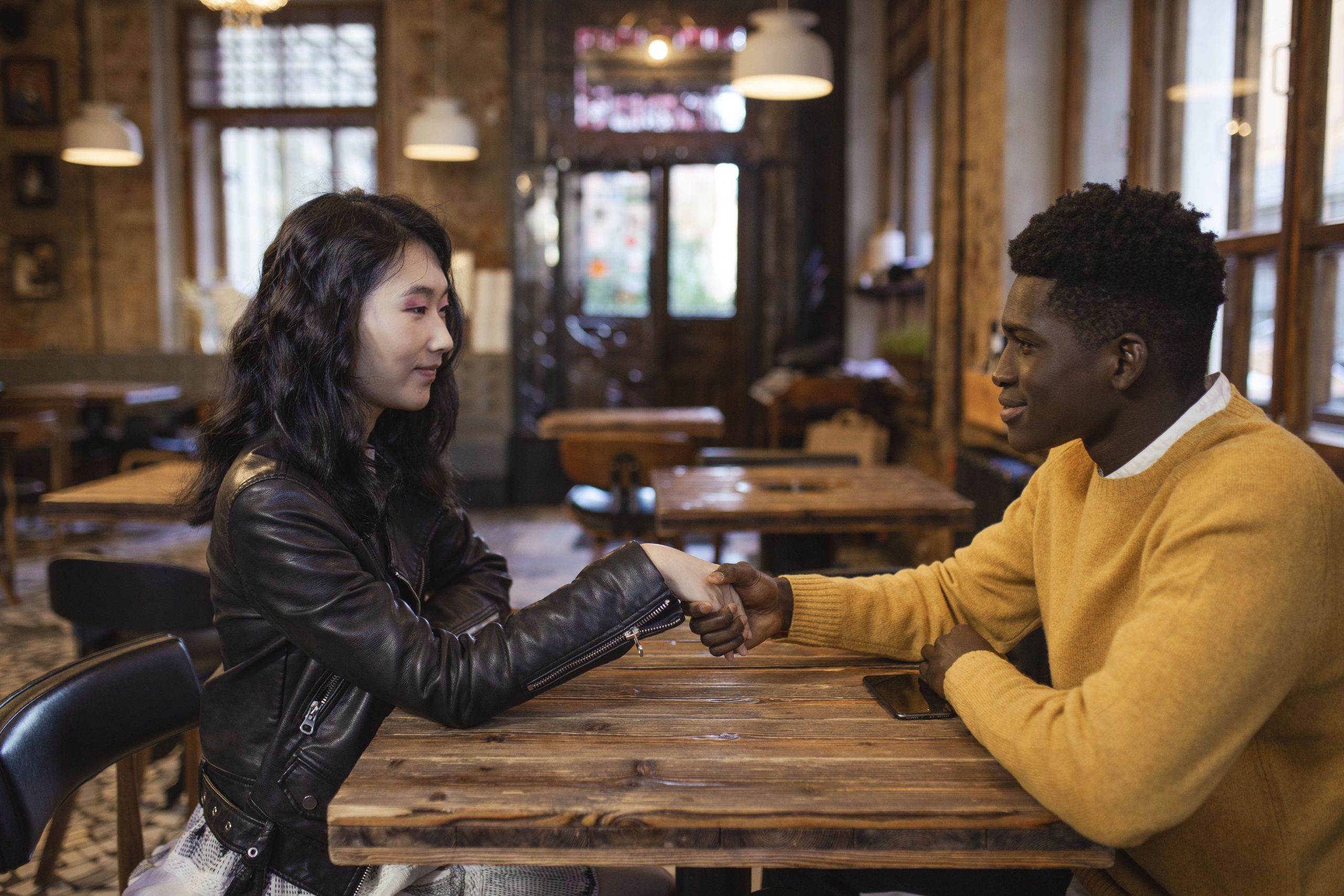 A man and woman smile and shake hands during a first meeting in a cafe.